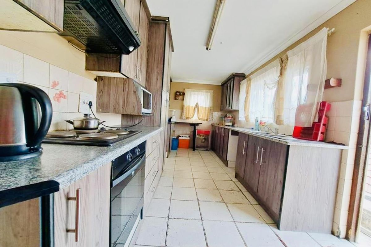 A functional galley-style kitchen featuring wood-look cabinetry, laminate countertops, built-in oven and hob, and tiled flooring throughout.