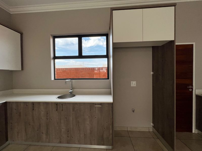 A clean, modern kitchen area featuring built-in cabinetry, a stainless steel sink, and a dedicated refrigerator alcove with tiled flooring.