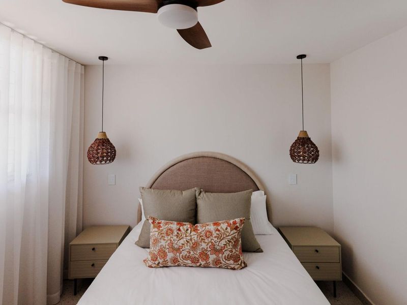 A well-appointed bedroom featuring a central ceiling fan, dual pendant lights, and floor-to-ceiling window treatments.