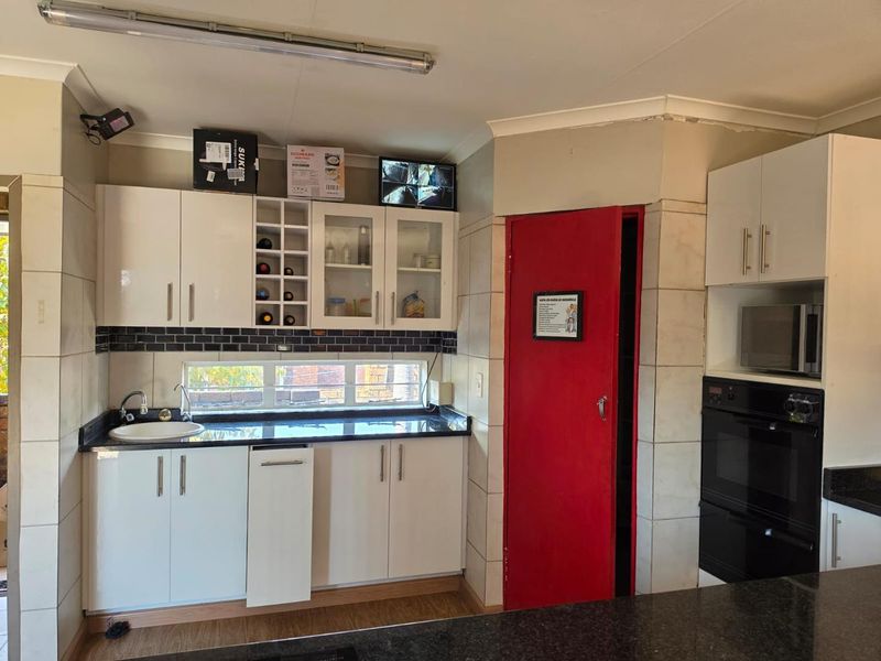 A functional kitchen featuring white cabinetry, dark granite countertops, built-in oven and microwave, and a tiled backsplash with a view through a horizontal window.