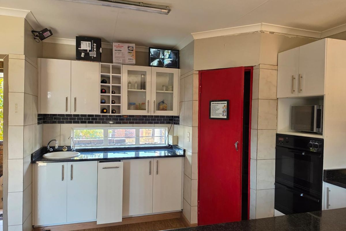 A functional kitchen featuring white cabinetry, dark granite countertops, built-in oven and microwave, and a tiled backsplash with a view through a horizontal window.