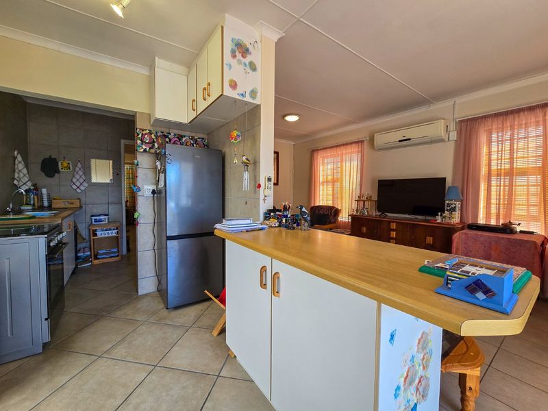 Open-plan living and kitchen area featuring tiled flooring, a breakfast bar, and a wall-mounted air conditioning unit.