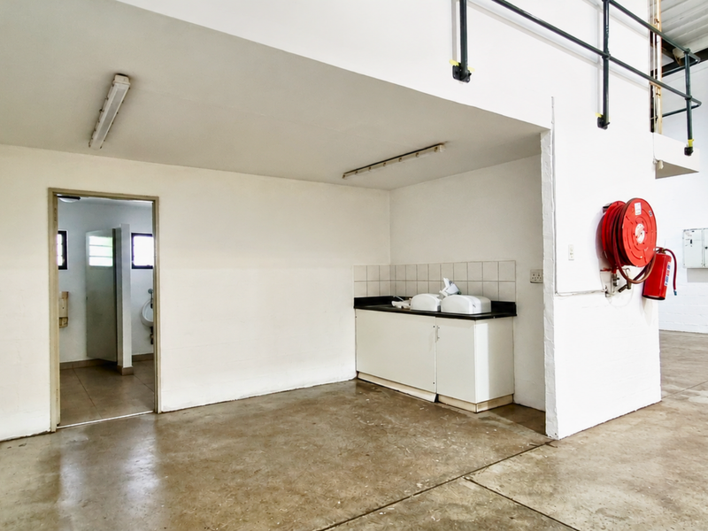 Industrial utility space featuring a kitchenette, fire safety equipment, and access to a restroom area with concrete flooring and mezzanine access.