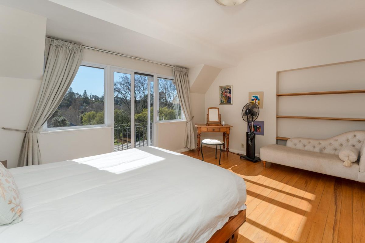 A bright bedroom featuring hardwood flooring, built-in shelving, and sliding glass doors that open onto a balcony with scenic views.