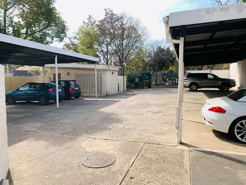 A paved outdoor parking area featuring covered carports, perimeter walling, and a secure gated entrance.