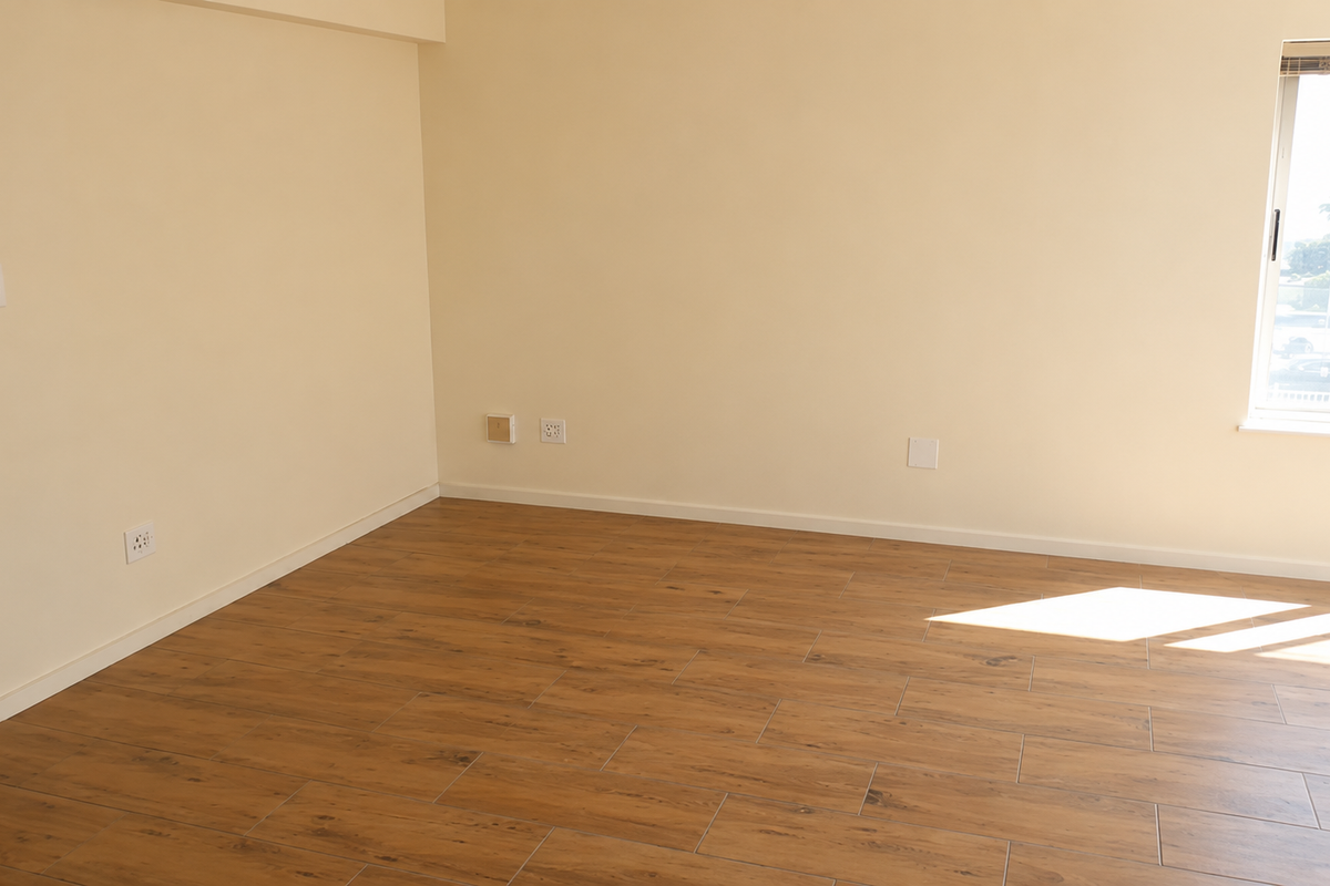 A bright, empty living area featuring modern wood-look tile flooring, neutral walls, and natural light from a side window.