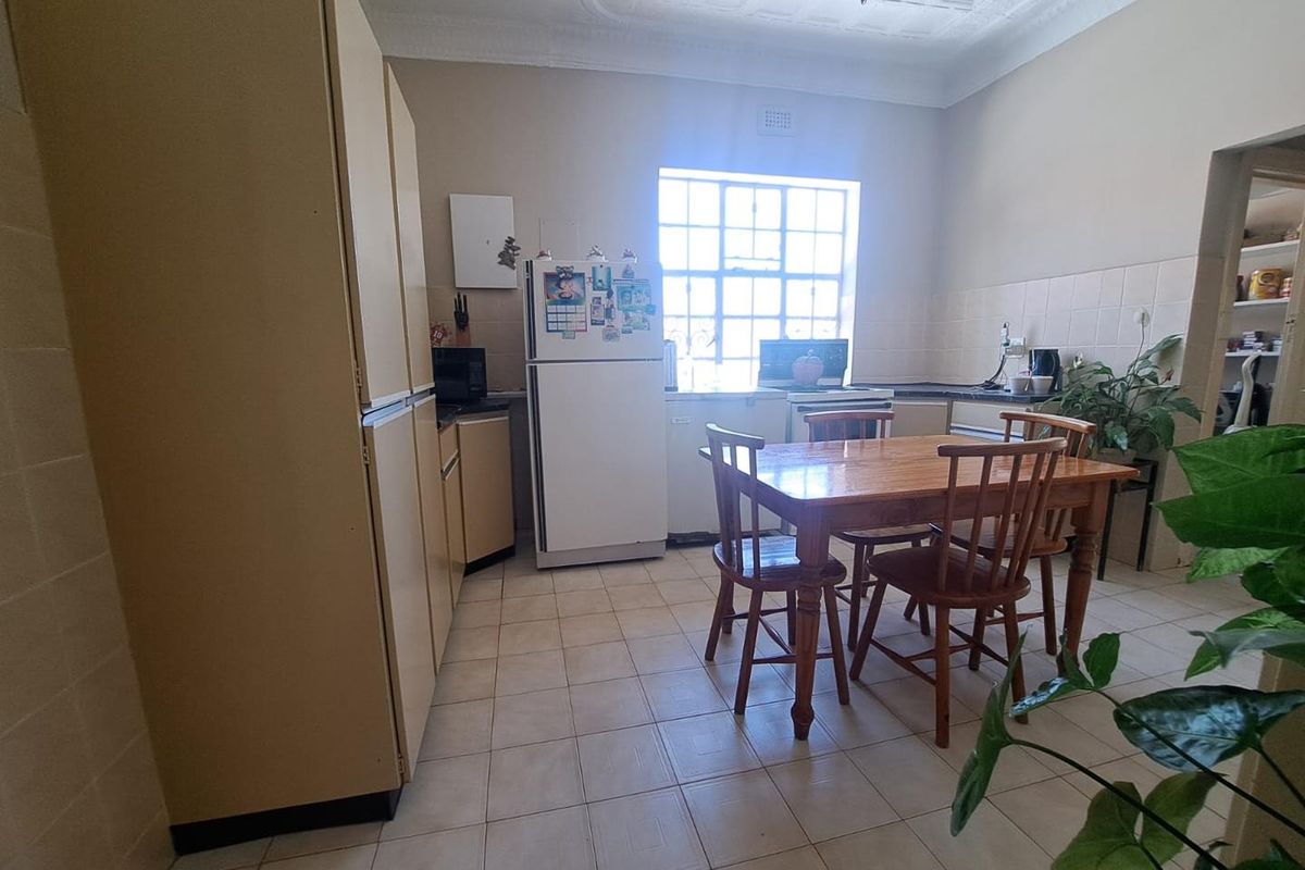 A dated kitchen featuring original cabinetry, tiled flooring, and a dedicated dining area with natural light from a large window.