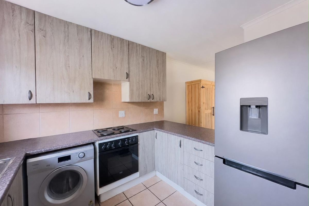 Functional kitchen featuring light wood-grain cabinetry, laminate countertops, tiled backsplash, and integrated electric cooking appliances with tiled flooring.