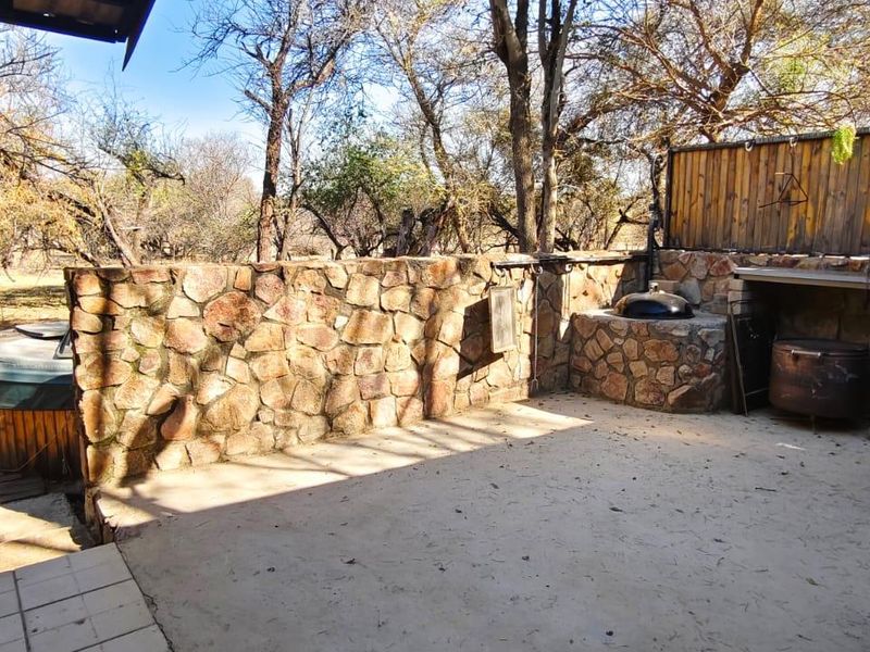 Outdoor patio area featuring a stone-clad wall, built-in braai, and integrated sink, set within a natural bushveld environment.
