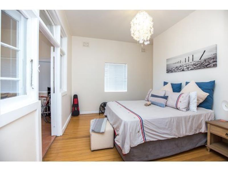 A bright bedroom featuring polished hardwood flooring, neutral walls, and a large window, providing a comfortable and well-maintained living space.