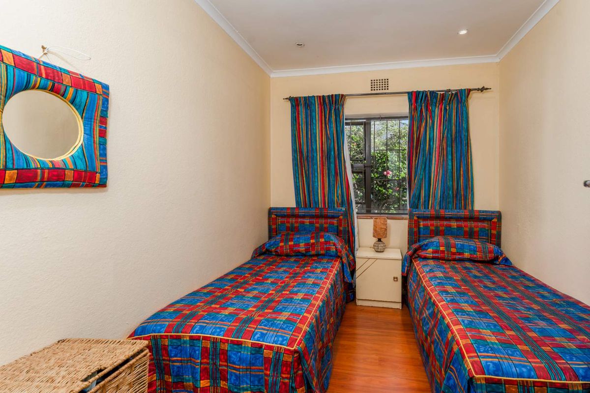 A compact bedroom featuring laminate flooring, recessed ceiling lighting, and a window with security bars.