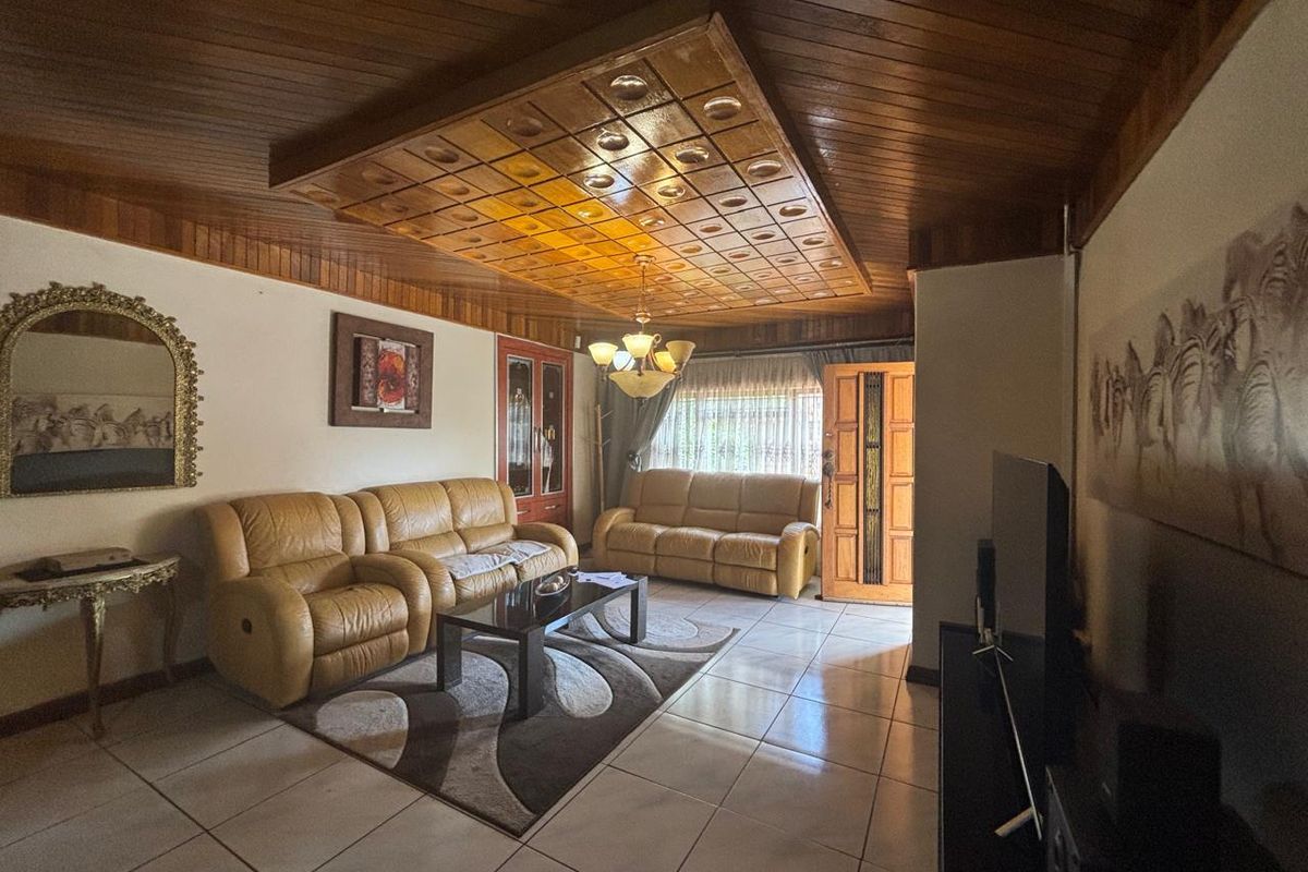 A living room featuring a distinctive coffered wood-paneled ceiling, tiled flooring, and a solid wood entrance door.