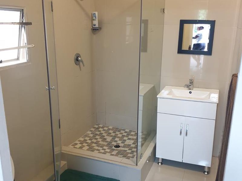 A functional bathroom featuring a glass-enclosed shower, a modern vanity with a basin, and neutral wall and floor tiling.
