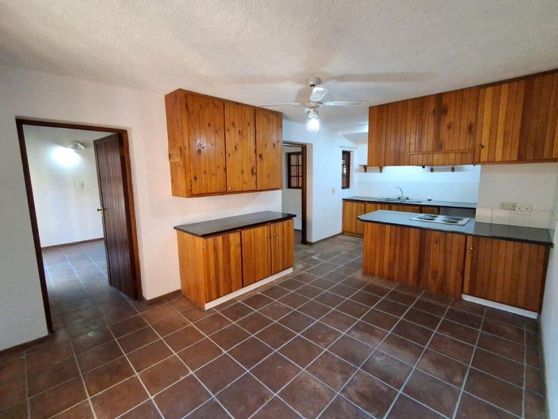 A spacious kitchen featuring wooden cabinetry, dark countertops, a built-in hob, and tiled flooring, offering a functional layout ready for modernization.