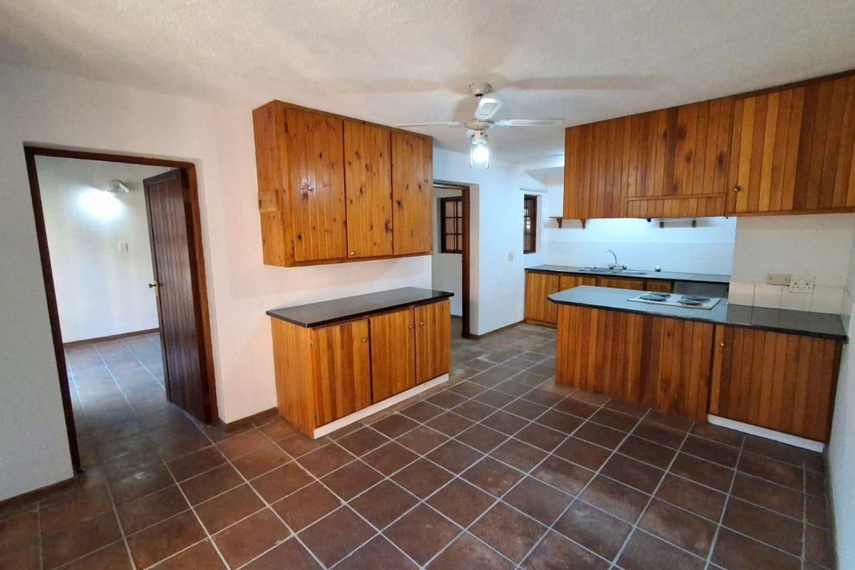 A spacious kitchen featuring wooden cabinetry, dark countertops, a built-in hob, and tiled flooring, offering a functional layout ready for modernization.