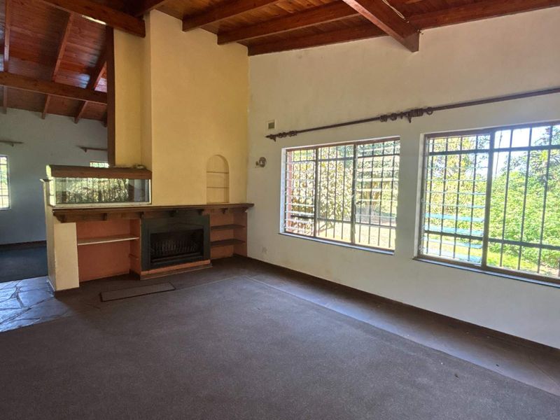 Spacious living room featuring a vaulted timber beam ceiling, a built-in fireplace, and large windows with security bars, offering a bright and open layout.