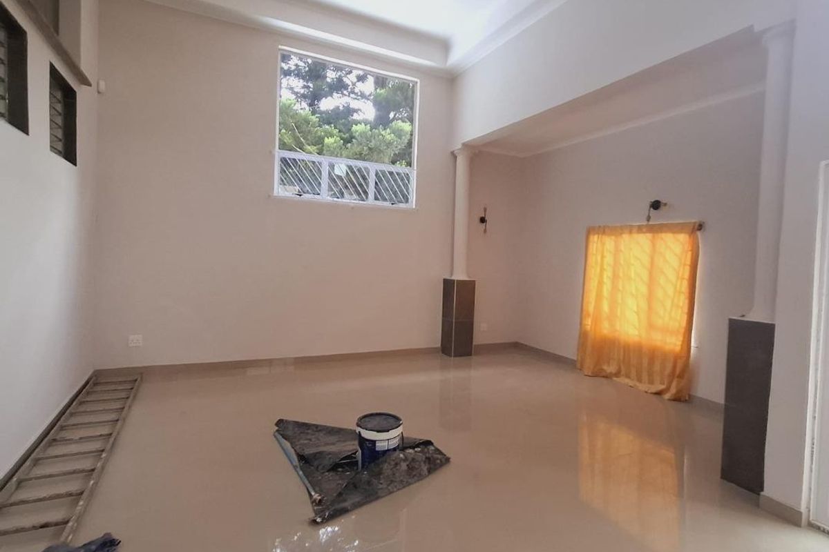 A spacious, empty living room featuring high ceilings, tiled flooring, and large windows that provide ample natural light.