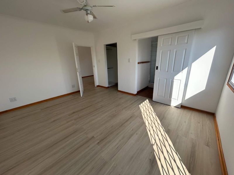 A bright, empty bedroom featuring modern laminate flooring, a ceiling fan, and access to an en-suite bathroom via a sliding door.