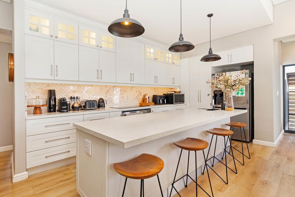 Modern kitchen featuring white cabinetry, stone countertops, a central island with breakfast bar seating, and a herringbone-patterned tiled backsplash.