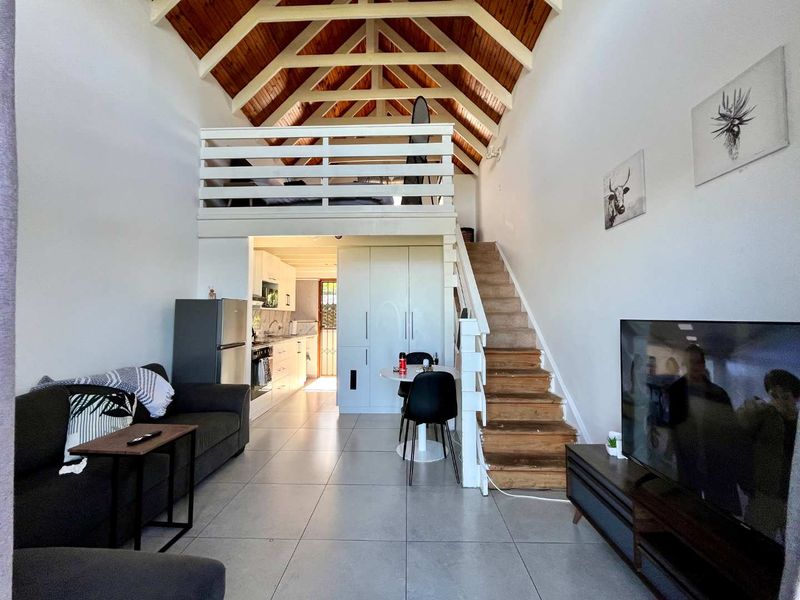 Open-plan living area featuring a vaulted timber ceiling, mezzanine loft level, tiled flooring, and an integrated kitchen space.