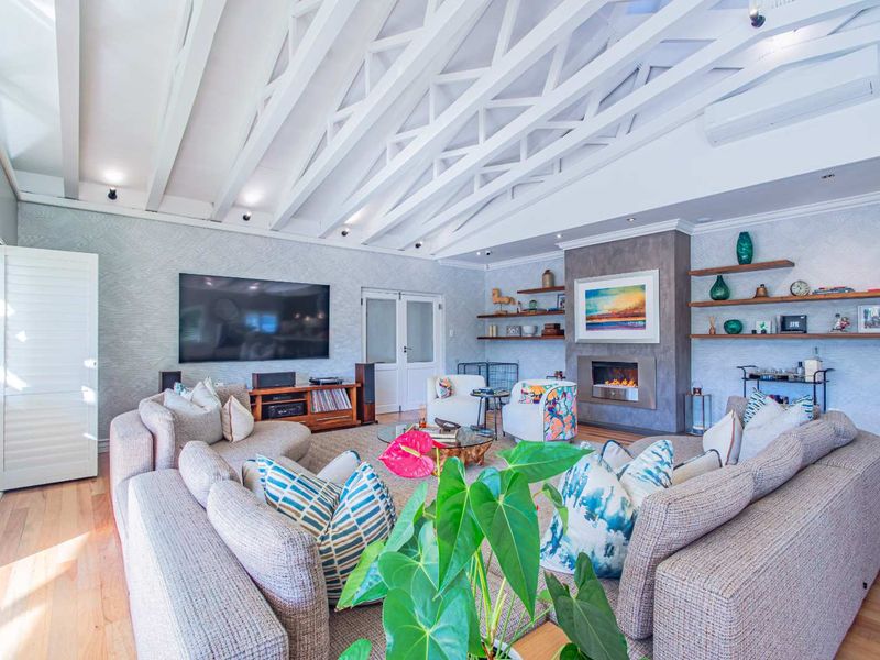 Spacious living room featuring a vaulted ceiling with exposed white trusses, hardwood flooring, and a modern built-in fireplace with floating shelving.