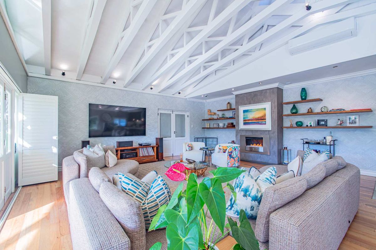 Spacious living room featuring a vaulted ceiling with exposed white trusses, hardwood flooring, and a modern built-in fireplace with floating shelving.