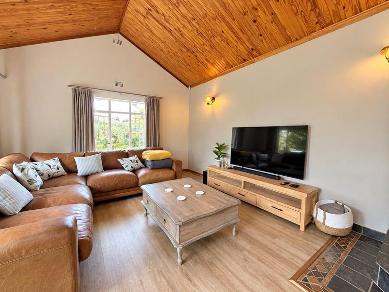Spacious living room featuring a high vaulted timber ceiling, laminate flooring, and a cozy tiled hearth area.