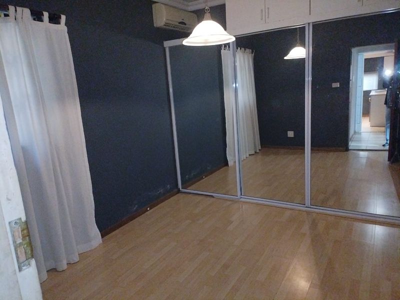A vacant bedroom featuring laminate flooring, a large built-in mirrored wardrobe with overhead storage, and a wall-mounted air conditioning unit.