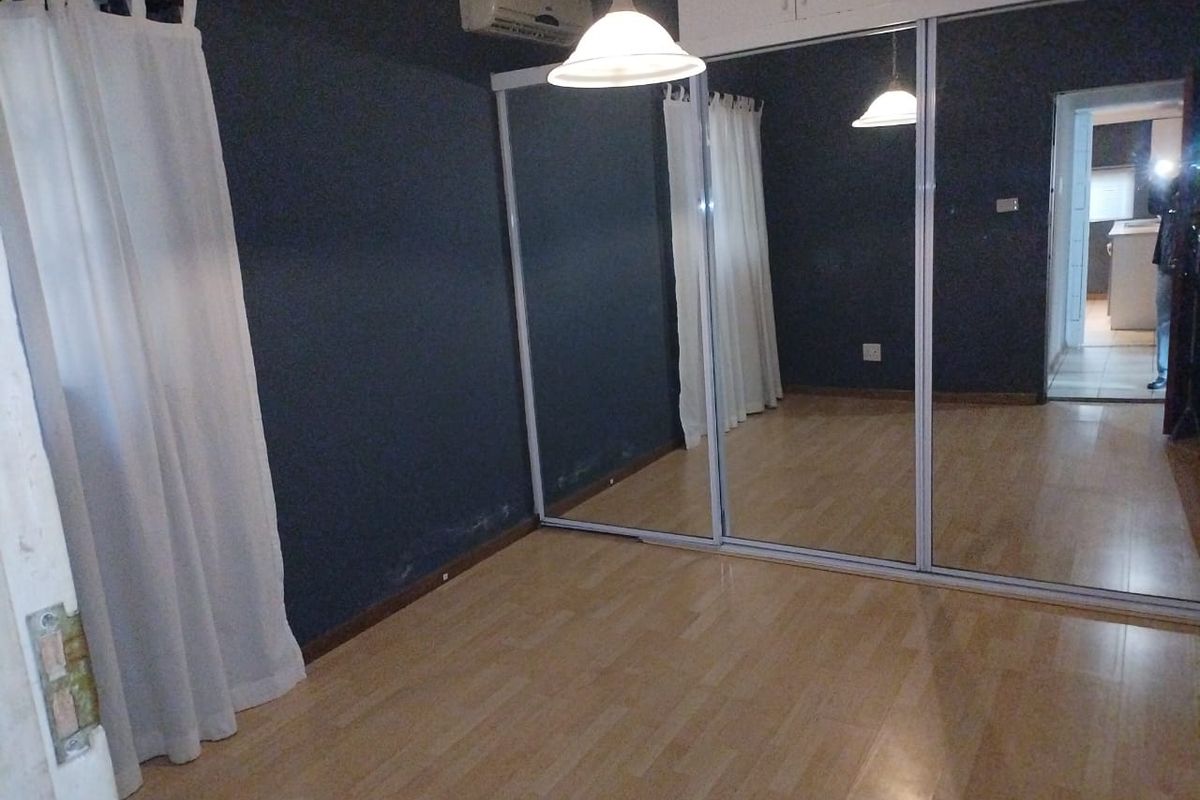 A vacant bedroom featuring laminate flooring, a large built-in mirrored wardrobe with overhead storage, and a wall-mounted air conditioning unit.