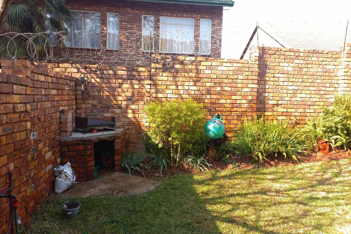A private rear garden featuring a built-in brick braai, enclosed by high brick boundary walls topped with security razor wire.