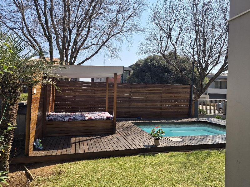 Outdoor pool area featuring timber decking, a built-in timber daybed structure, and a privacy screen, set within a private garden space.
