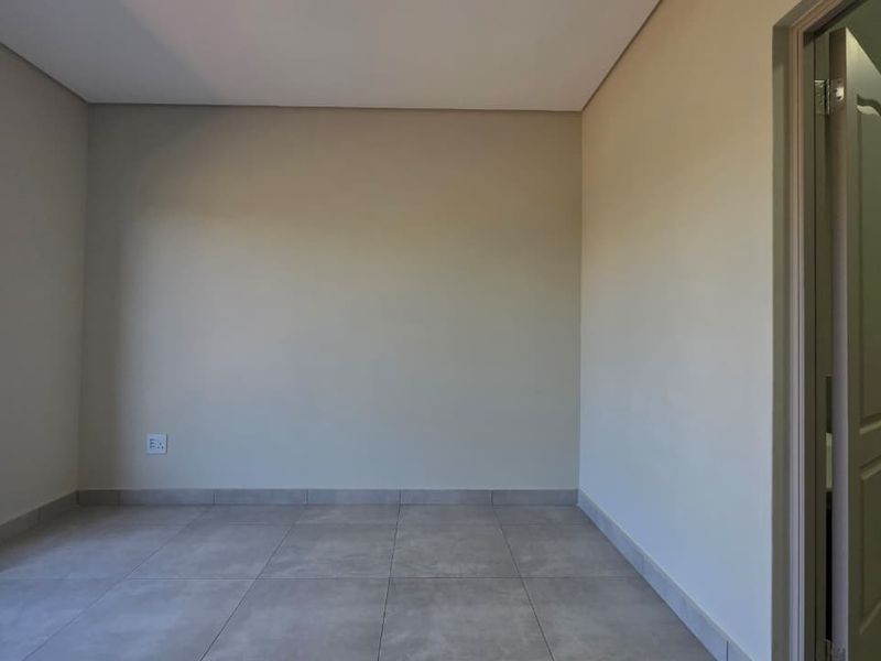 A bright, empty bedroom featuring neutral wall tones, large window, and modern tiled flooring, providing a clean canvas for personalization.
