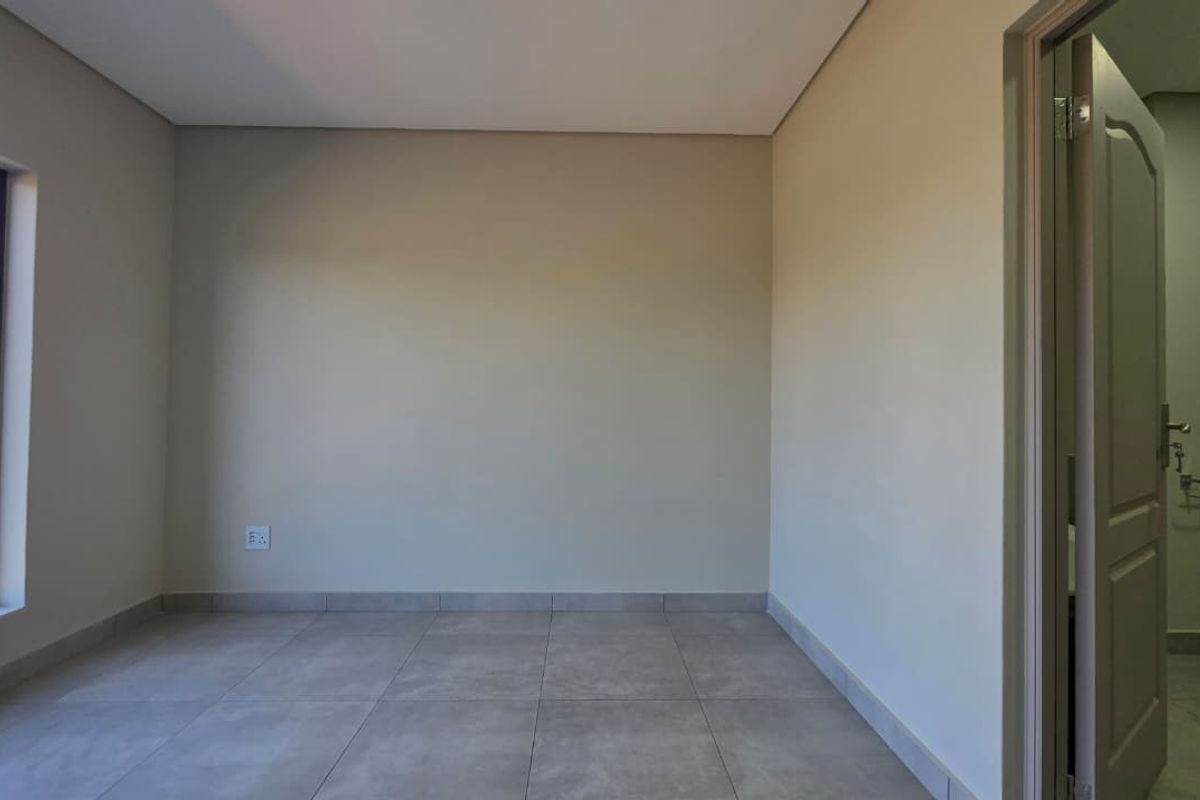 A bright, empty bedroom featuring neutral wall tones, large window, and modern tiled flooring, providing a clean canvas for personalization.