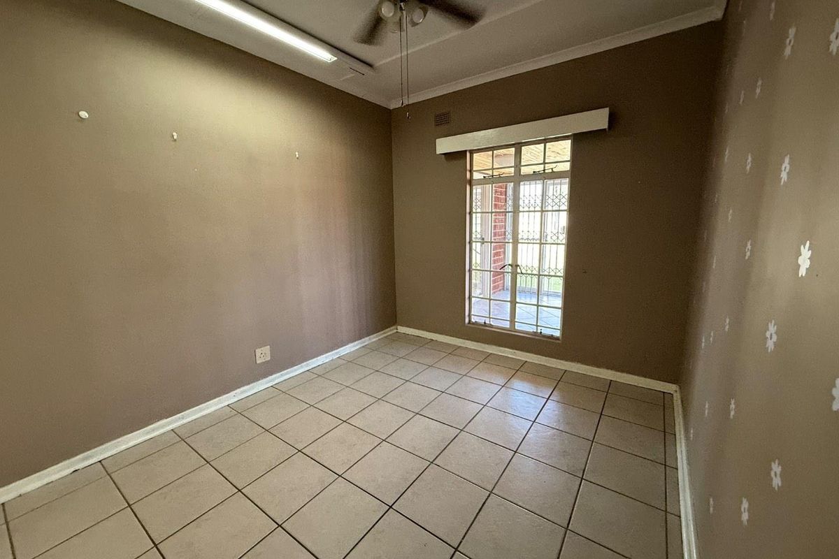 An empty bedroom featuring tiled flooring, a ceiling fan, and a window with security bars, offering a blank canvas for potential updates.