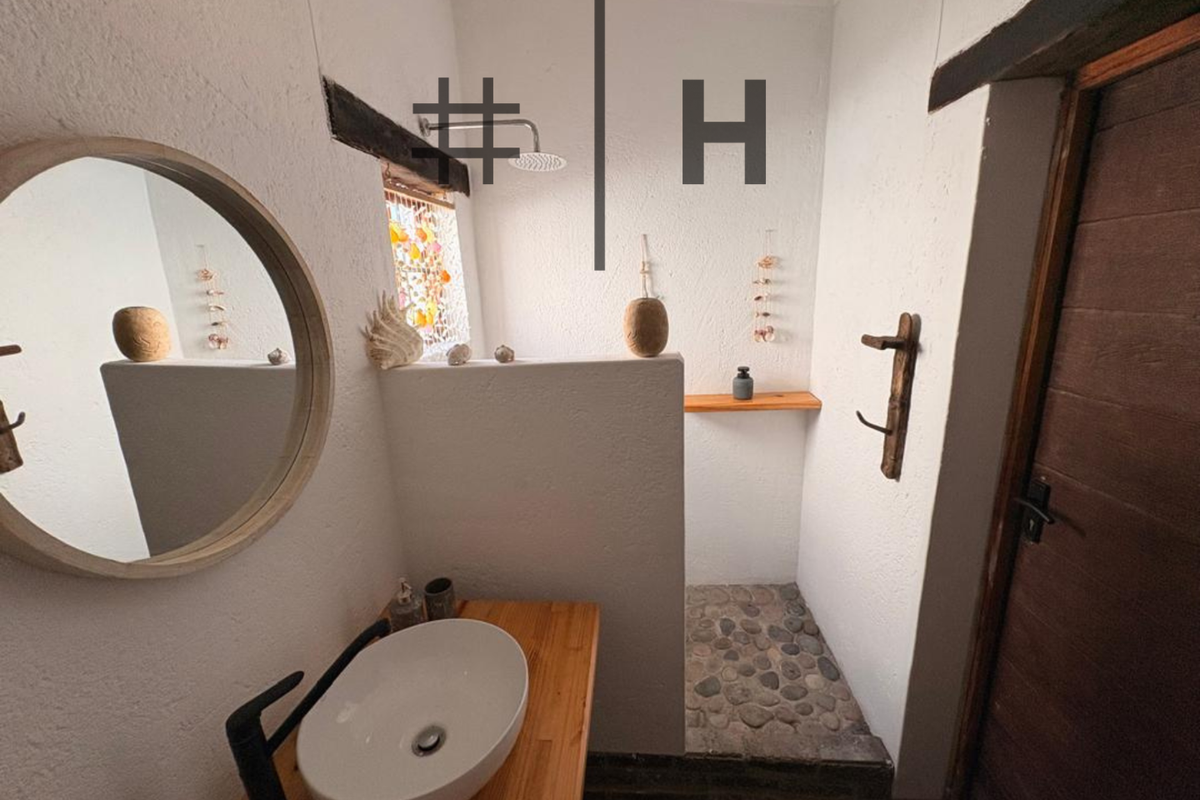 A rustic-style bathroom featuring a vessel sink on a wooden vanity, a walk-in shower with a pebble floor, and a wooden door.