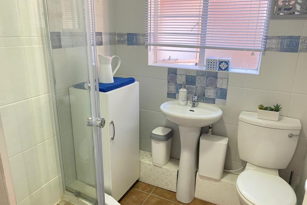 A compact bathroom featuring a glass-enclosed shower, pedestal basin, and toilet with tiled walls and flooring.