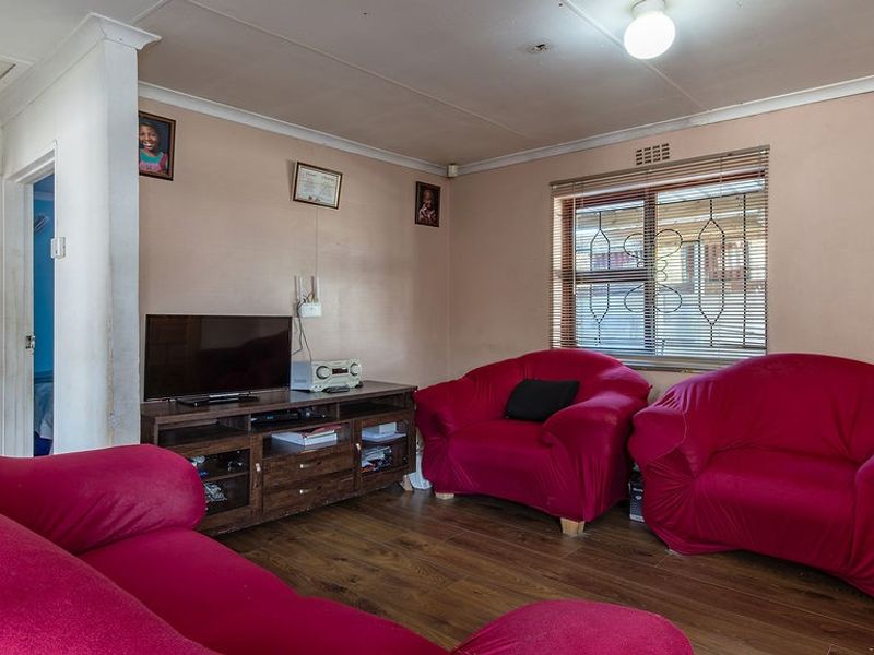A living room featuring laminate flooring, coved ceilings, and security burglar bars on the window, providing a functional and lived-in space.
