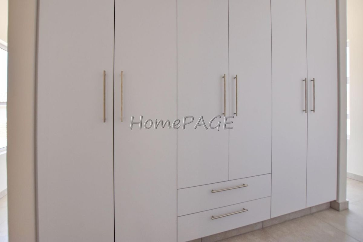A bedroom featuring floor-to-ceiling built-in wardrobes with modern handles and integrated drawers, providing ample storage space.
