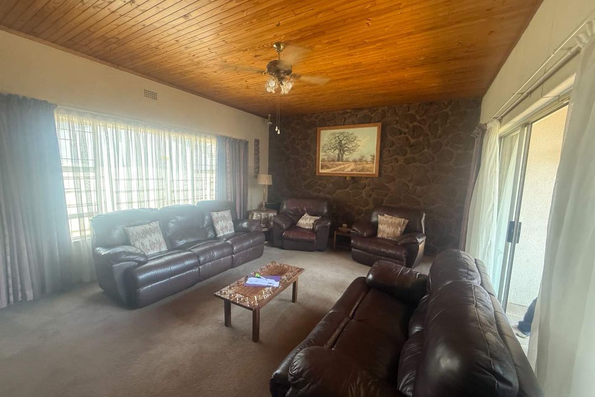 A living room featuring a distinctive stone accent wall, timber-clad ceiling, ceiling fan, and large windows providing natural light with access to an outdoor area.