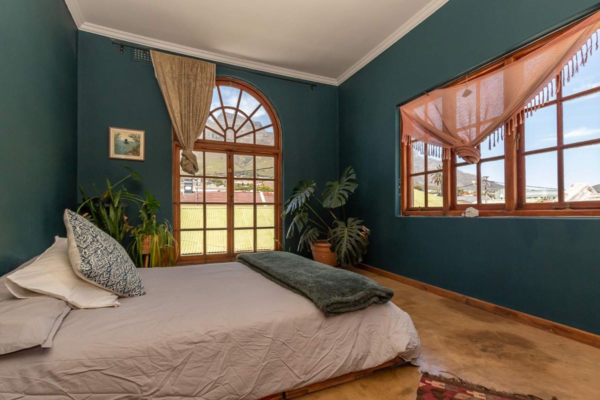 A bedroom featuring dark teal walls, arched wooden-framed glass doors, and large windows with mountain views, finished with polished concrete flooring.
