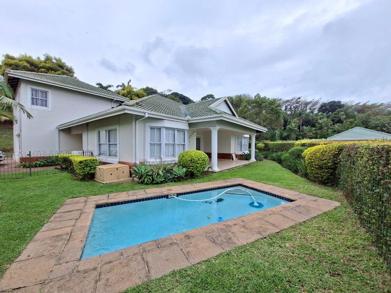 Rear view of the townhouse featuring a private swimming pool, covered patio area, and established garden surroundings.