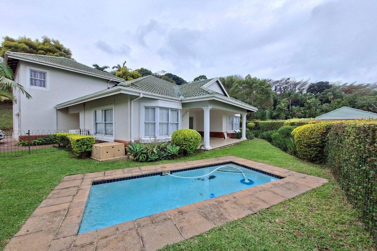 Rear view of the townhouse featuring a private swimming pool, covered patio area, and established garden surroundings.