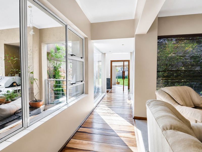 A bright, modern hallway featuring polished timber flooring, expansive glass windows, and a seamless transition to the outdoor area.