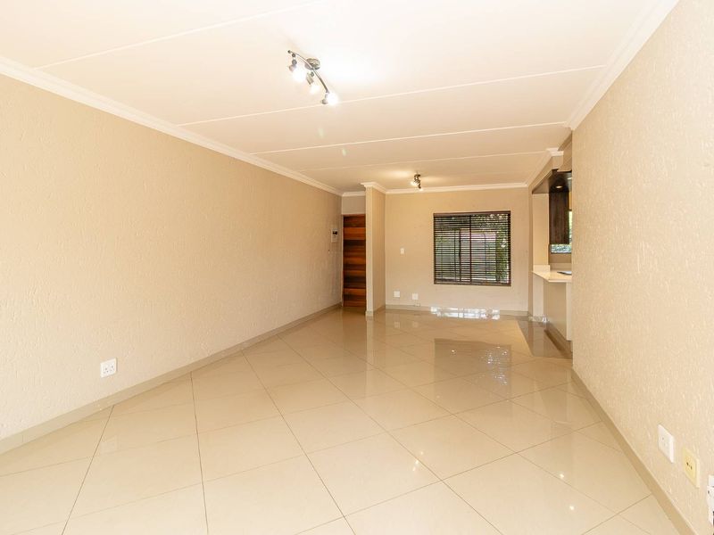 Spacious open-plan living area featuring neutral tiled flooring, coved ceilings, and a breakfast bar connecting to the kitchen space.