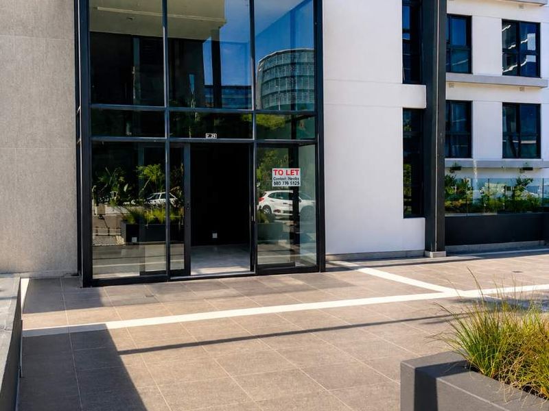 Modern retail storefront entrance featuring a large glass facade, tiled patio area, and contemporary concrete planter boxes.