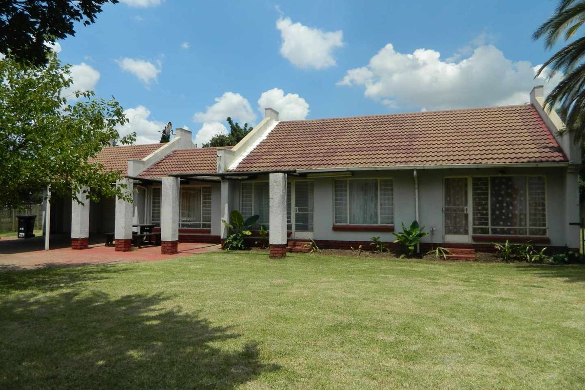 Rear view of a single-story house featuring a tiled roof, concrete pillars, a paved patio area, and a spacious lawn.