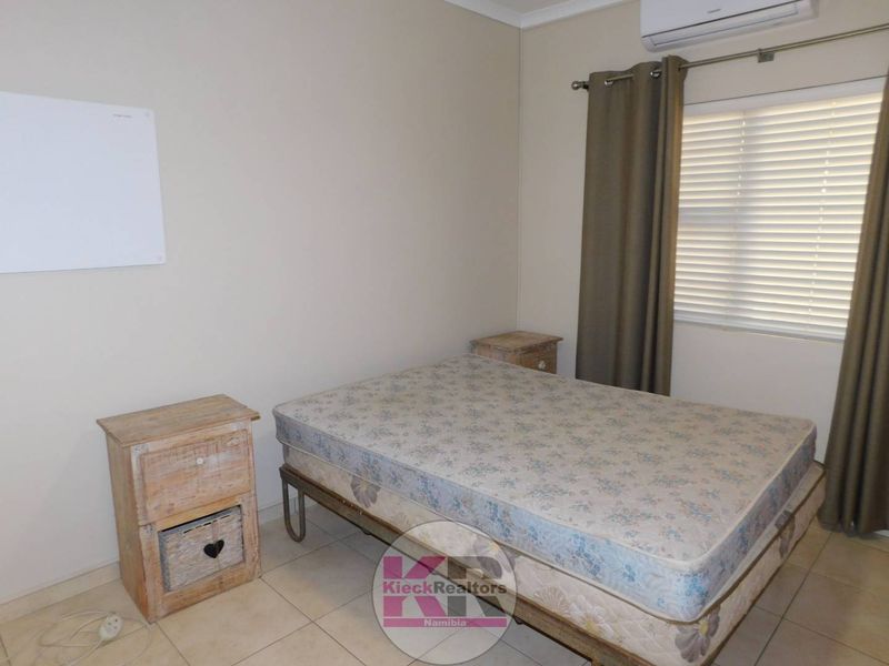 A functional bedroom featuring tiled flooring, an installed air conditioning unit, and window blinds.