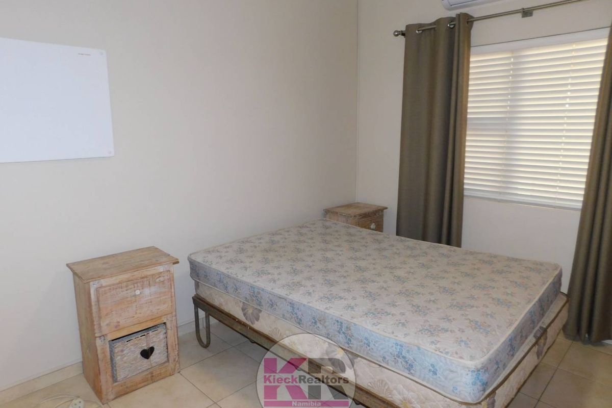 A functional bedroom featuring tiled flooring, an installed air conditioning unit, and window blinds.