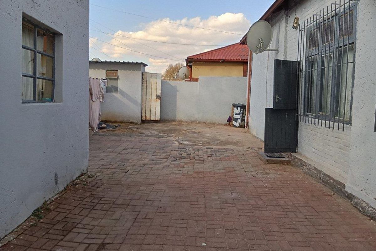 A paved rear courtyard area enclosed by boundary walls, featuring security bars on windows and a satellite dish installation.
