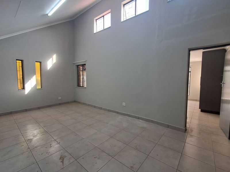 An empty, spacious living area featuring high raked ceilings, tiled flooring, and multiple windows with security bars, offering a blank canvas for interior design.